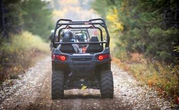 A group of people ride ORVs single file down a wooded trail.