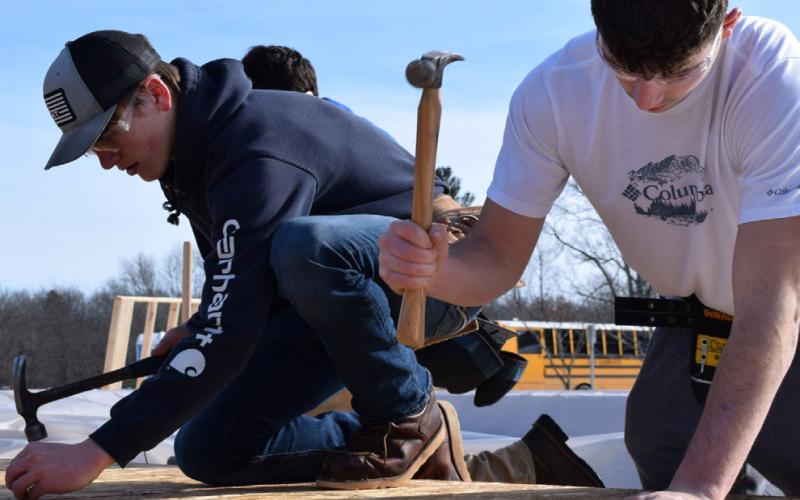 Pictured at left, Megan Veitengruber, Clare-Gladwin CTE Student from Clare High School, holds one of the Agricultural Science program’s recently born piglets. At right, Construction Trade students begin framing and setting trusses on modular home for Gladwin County Land Bank.