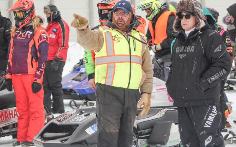 Volunteers discuss when it’s time for the next green flag to drop prior to one of the Vintage Snowmobile Races Saturday.