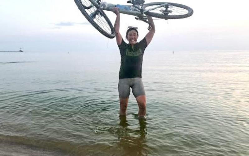 Katie Keen holding her bicycle in the air after she crosses the finish line at Lake Michigan.