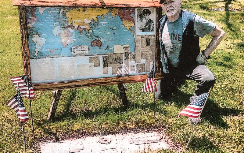 Gladwin’s Harry Riopelle poses at the gravesite of David Fleming Jr. with the display he created after purchasing a collection of antiques and finding an envelope containing a detailed account of Fleming’s exploits as an airman during World War II.