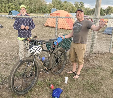 DALMAC ride cyclist Keith Buchley (right) of Lansing relaxes before spending Thursday night in the parking lot at Gladwin High School on his way to Mackinaw City.