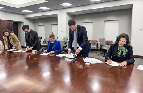 Secretary of State Jocelyn Benson (center) and Gov. Gretchen Whitmer (right) are assisted by staff members as they sign Certificates of Ascertainment for the 2024 Presidential Election.