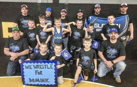 Members of the Gladwin Youth Wrestling organization and their coaches gather for a team picture with the sign honoring Dominic Haines that they took with them to the recent state tournament in Traverse City.