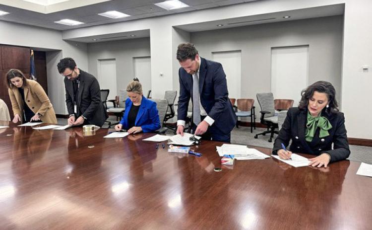 Secretary of State Jocelyn Benson (center) and Gov. Gretchen Whitmer (right) are assisted by staff members as they sign Certificates of Ascertainment for the 2024 Presidential Election.