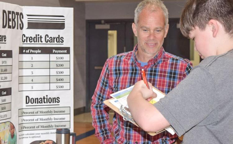 Reality Store volunteer Chris Pellerito from Mid Michigan College talks to Gladwin eighth-grade students about child care expenses, student loans, credit card debt and donations.