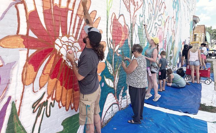 Street Fest attendees helping to finish the mural on the Edward Jones Financial Advisory building on Cedar Ave. GLADWIN