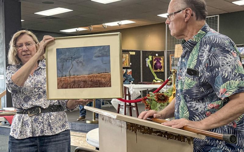 Jan Berg-Rezmer holds Connie Maedel Diehl’s painting while 2025 Art Judge Lynn Morgan comments as to why he chose the pastel titled, Forgotten Pasture, for a third place award in the General Art category.