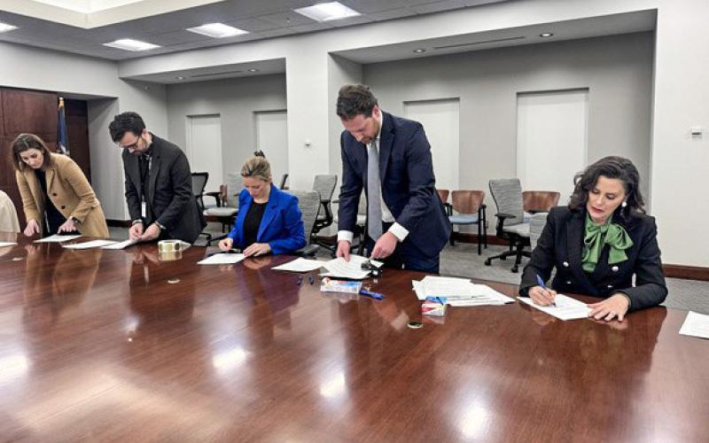 Secretary of State Jocelyn Benson (center) and Gov. Gretchen Whitmer (right) are assisted by staff members as they sign Certificates of Ascertainment for the 2024 Presidential Election.