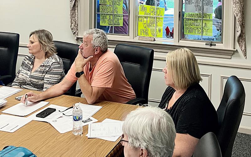 The signs of the times are displayed in the window of City Hall behind (left to right) City Administrator Kimberly Hines andCouncil Members John Caffrey and Jaimie Esiline during Monday night’s Regular Meeting.