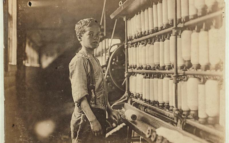 John Dempsey, said to be 12-years-old, working in the mule-spinning room at Jackson Mill, Fiskeville, R.I. in 1909. PHOTO BY LEWIS WICKES HINE FOR THE NATIONAL CHILD LABOR COMMITTEE