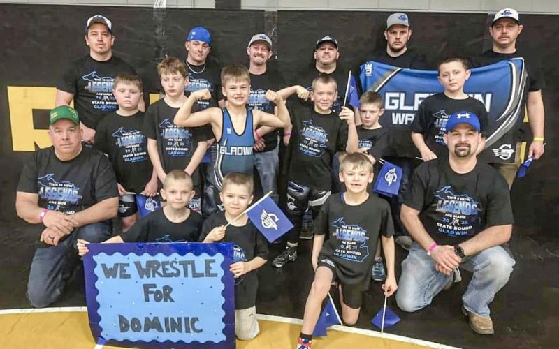 Members of the Gladwin Youth Wrestling organization and their coaches gather for a team picture with the sign honoring Dominic Haines that they took with them to the recent state tournament in Traverse City.