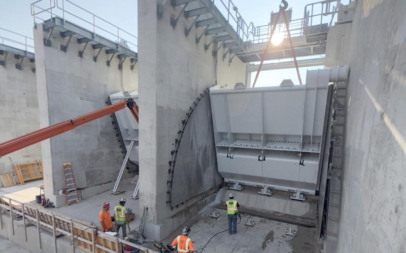 The next three milestones for Sanford are installation of the dam gates, I-wall top cap, and roller compacted concrete (RCC) wall, which is scheduled for the fall. July had more rain events than usual which slowed down gate installation. The team was able to set gate #1 by the end of July. The I-wall is a flood control wall that attaches to sheet pile in the ground. Installation of the concrete top cap is ongoing. The RCC wall installation began and is expected to continue through the fall.