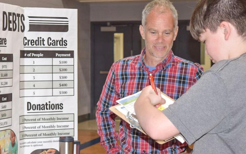 Reality Store volunteer Chris Pellerito from Mid Michigan College talks to Gladwin eighth-grade students about child care expenses, student loans, credit card debt and donations.