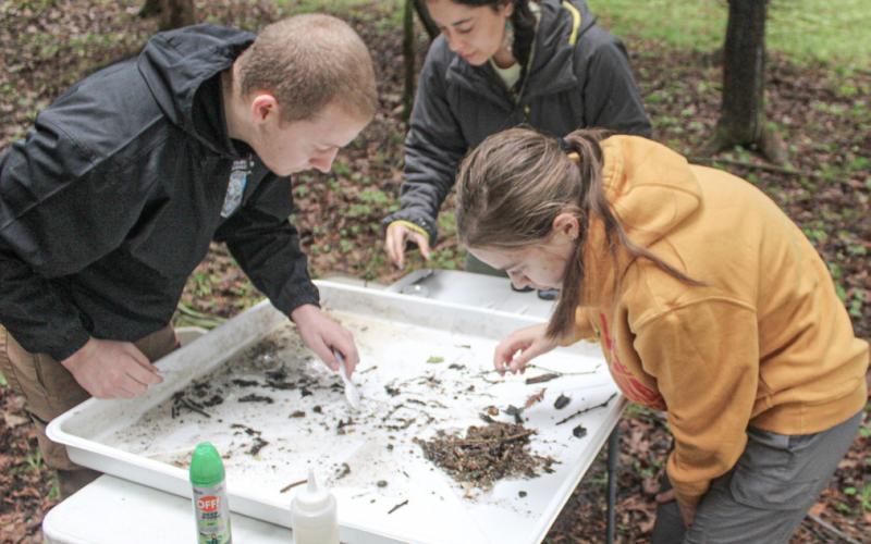 Material from the riverbed is examined by (left to right) Riley Hayer, Lily Kelsey and Meredith McCulloch at a station set up on shore.