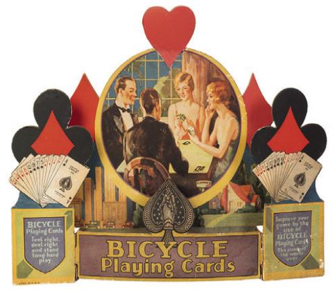 When advertisements include pictures of people, their clothing and hairstyles can help date the item. This store display for Bicycle Playing Cards is from about 1930. KOVELS.COM