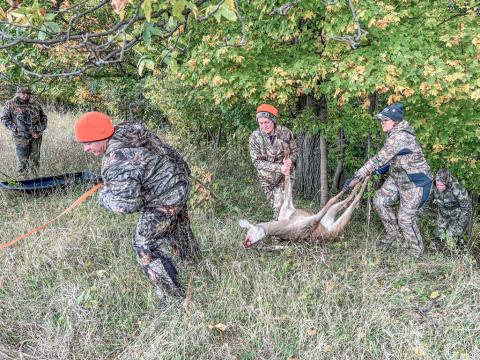 Women work together to drag a harvested deer up a steep embankment.