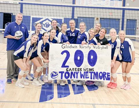 The Gladwin volleyball team celebrates with Coach Tony Wetmore after delivering his 200th career victory last Wednesday by sweeping visiting Standish.
