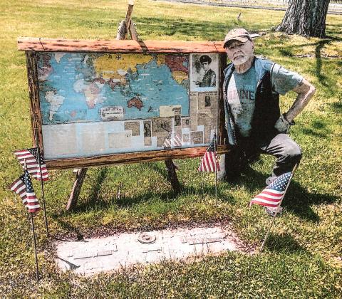 Gladwin’s Harry Riopelle poses at the gravesite of David Fleming Jr. with the display he created after purchasing a collection of antiques and finding an envelope containing a detailed account of Fleming’s exploits as an airman during World War II.