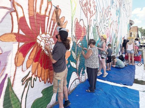 Street Fest attendees helping to finish the mural on the Edward Jones Financial Advisory building on Cedar Ave. GLADWIN