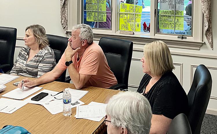 The signs of the times are displayed in the window of City Hall behind (left to right) City Administrator Kimberly Hines andCouncil Members John Caffrey and Jaimie Esiline during Monday night’s Regular Meeting.