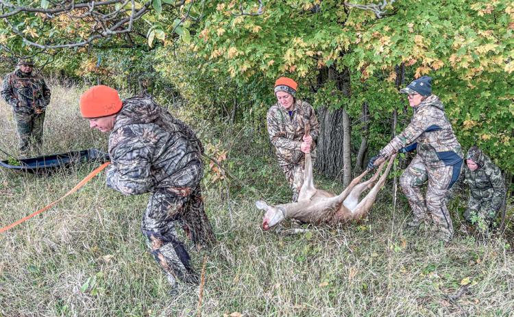 Women work together to drag a harvested deer up a steep embankment.
