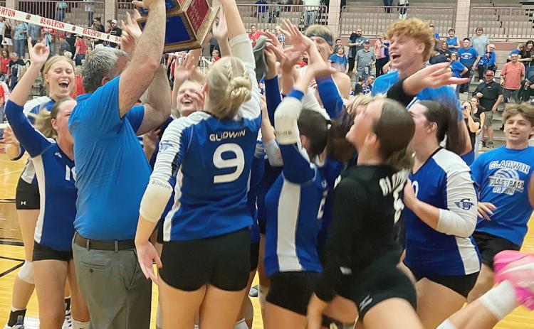 Gladwin coach Tony Wetmore holds the Cedar Cup aloft as his team celebrates after beating Beaverton in five sets last week to retain possession of the trophy.