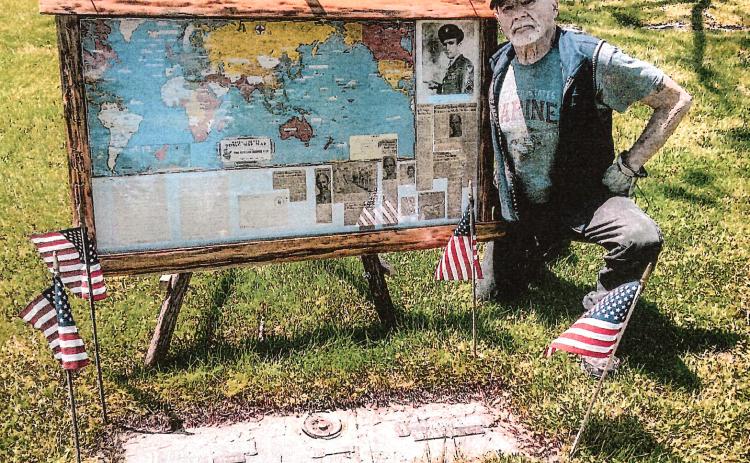 Gladwin’s Harry Riopelle poses at the gravesite of David Fleming Jr. with the display he created after purchasing a collection of antiques and finding an envelope containing a detailed account of Fleming’s exploits as an airman during World War II.