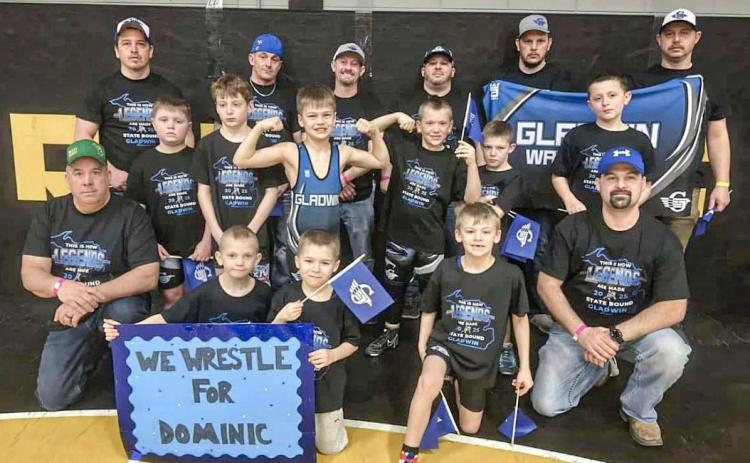 Members of the Gladwin Youth Wrestling organization and their coaches gather for a team picture with the sign honoring Dominic Haines that they took with them to the recent state tournament in Traverse City.
